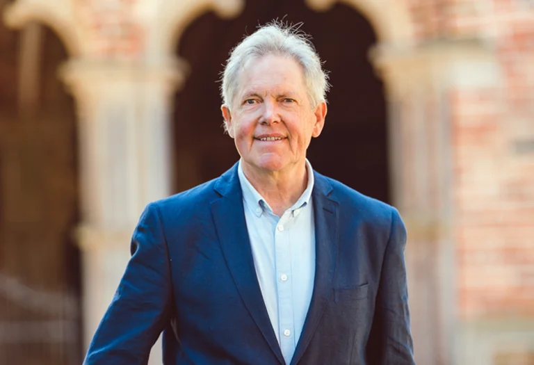 Ein Mann mit kurzen grauen Haaren, Brille und einem dunkel blauen Sakko lächelt in die Kamera